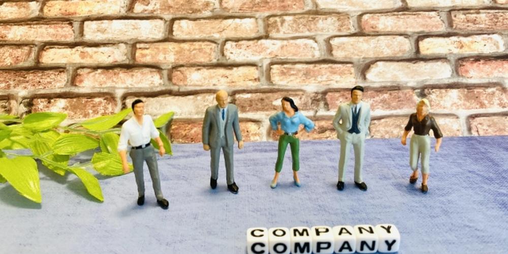 レンガの背景に5人のビジネスマン風ミニチュアが並び、「COMPANY」の文字ブロックが配置された会社の雰囲気を表す構図。