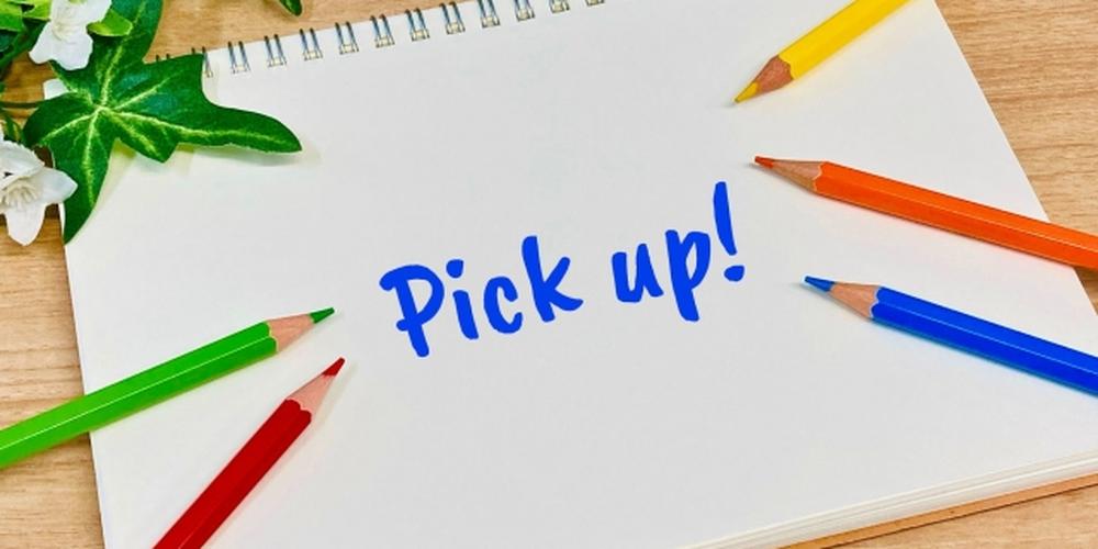 カラフルな色鉛筆に囲まれたノートに「Pick up!」と青文字で書かれている画像