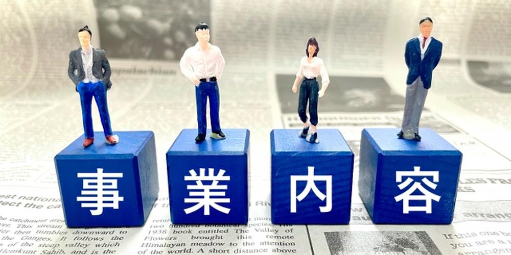 新聞の上に置かれた青いブロックに「事業内容」と書かれ、4人のフィギュア