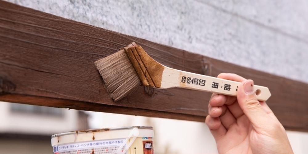木材に茶色の塗料を塗っている刷毛と手元のクローズアップ