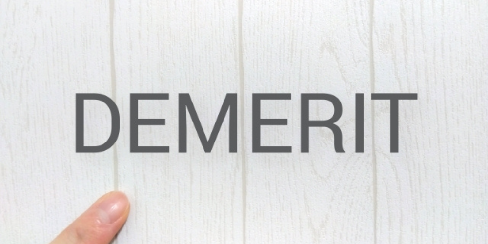 木目背景に「DEMERIT」と書かれた文字と人の指先