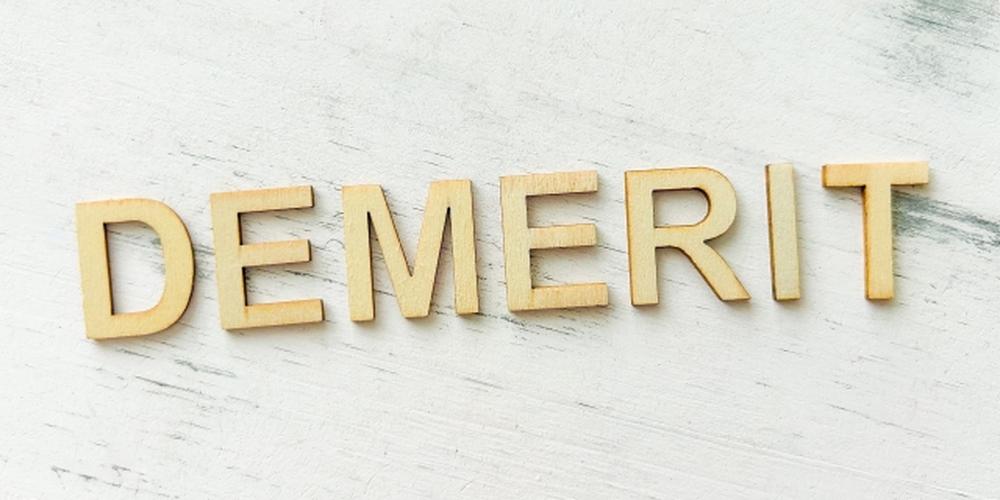 「DEMERIT」の文字が木製のアルファベットで並べられ、白い木目調の背景が映えるデメリットの表現。
