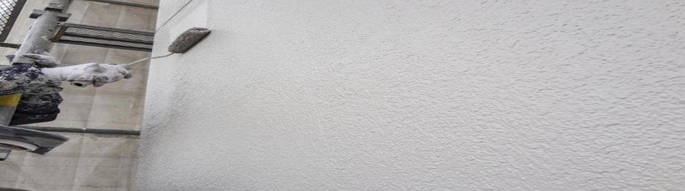 外壁をローラーで白く塗装している作業員の手元
