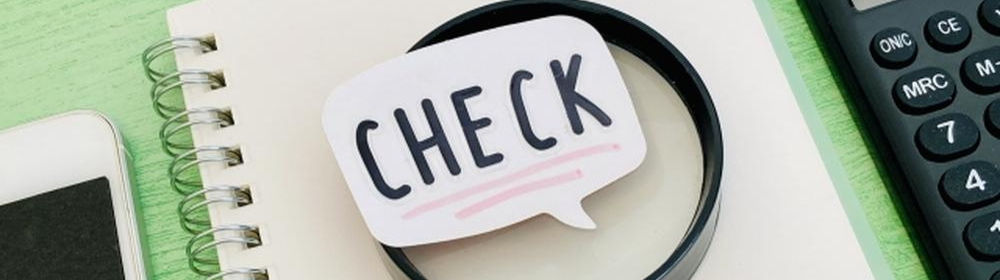 ノートの上に虫眼鏡と「CHECK」の吹き出し、電卓など