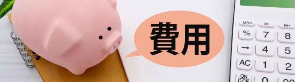 電卓とノートの間に置かれたピンク色の貯金箱と「費用」の吹き出し