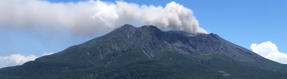 噴煙を上げる桜島を錦江湾越しに望む