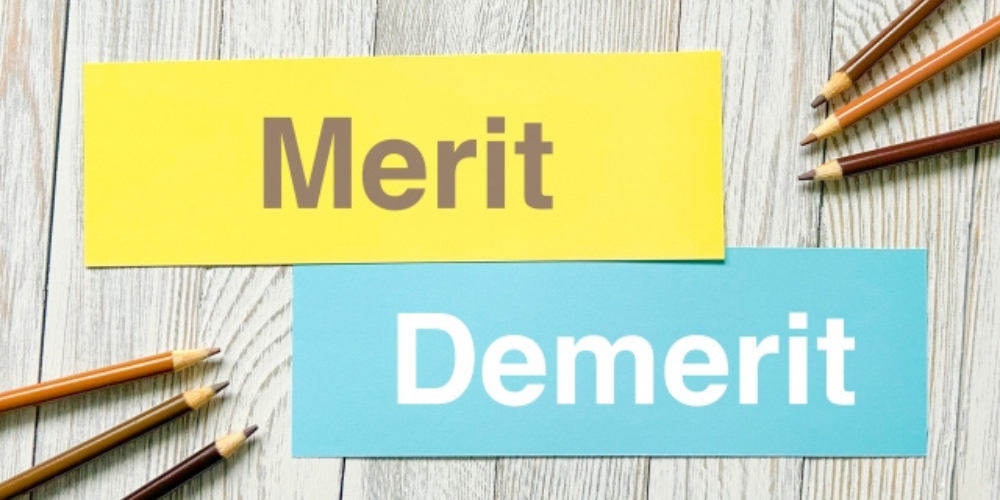 木目の背景に「Merit」と「Demerit」と書かれた紙が並ぶイメージ、周囲に鉛筆